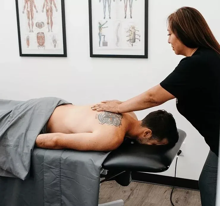 A licensed massage therapist working the mid-back of a patient lying prone under a sheet